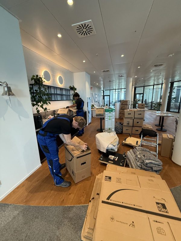 Mitarbeiter schließt einen Umzugskarton in einem Büro, im Hintergrund stehen weitere gepackte Kisten