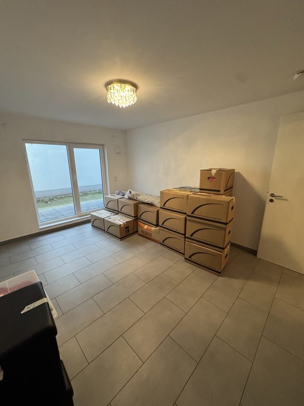 Gestapelte Umzugskartons in einem leeren Neubauzimmer mit bodentiefem Fenster