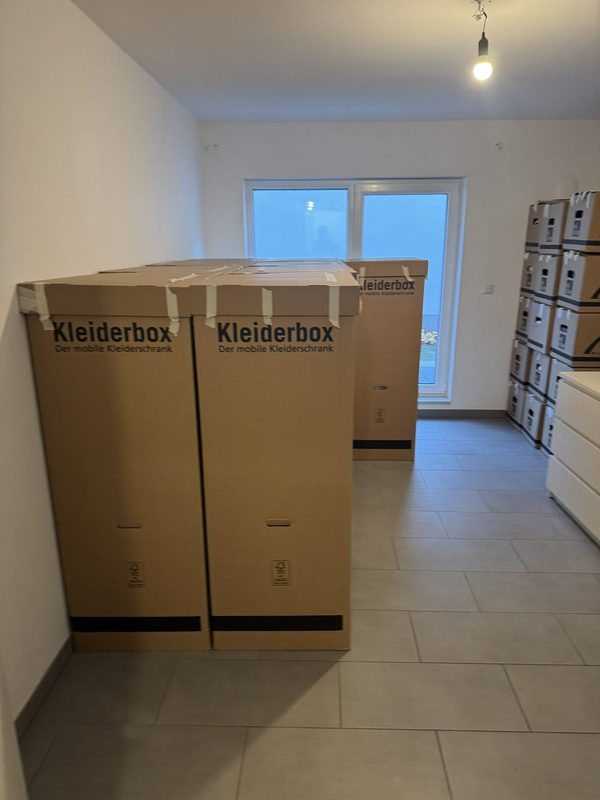 Zwei Kleiderboxen und Kartonstapel stehen in einem leeren Zimmer