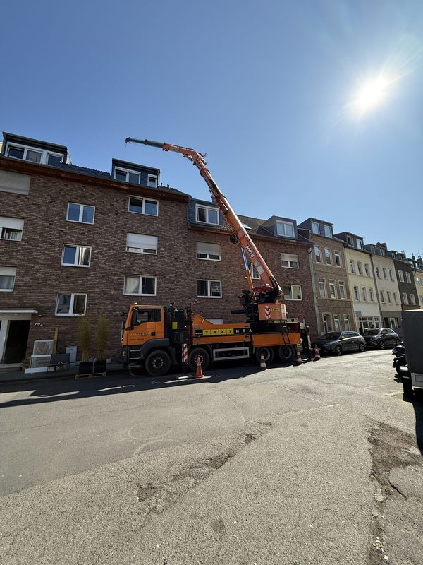 Orangefarbener Kranwagen steht mit ausgefahrenem Ausleger und Warnkegeln in einer Wohnstraße