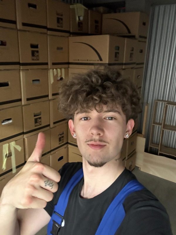 Mitarbeiter steht vor einer Wand aus fertig gepackten und beschrifteten Umzugskartons