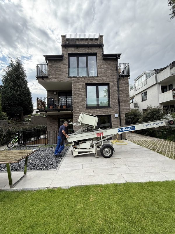 Mitarbeiter richtet einen Möbellift auf einer Einfahrt vor einem Wohnhaus aus