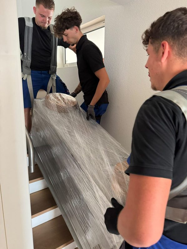 Drei Mitarbeiter tragen ein foliertes Möbelstück gemeinsam eine Treppe hinunter