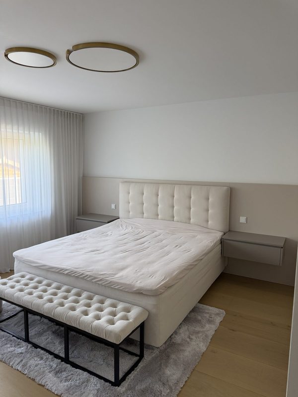 Helles Schlafzimmer mit aufgebautem Boxspringbett und Sitzbank am Fußende