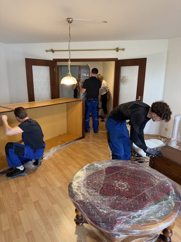 Vier Mitarbeiter setzen gemeinsam den Korpus einer großen Schrankwand in einem Wohnzimmer zusammen