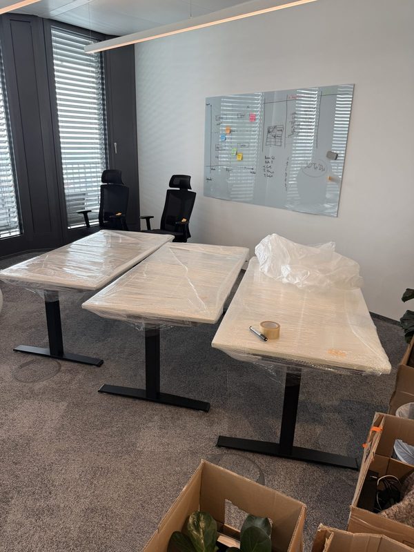 Drei höhenverstellbare Schreibtische stehen mit folierten Platten nebeneinander in einem Büro
