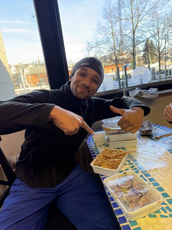 Mitarbeiter sitzt in der Mittagspause an einem Tisch und zeigt auf das Essen vor sich