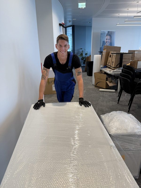Mitarbeiter steht hinter einer großflächig mit Luftpolsterfolie verpackten Tischplatte