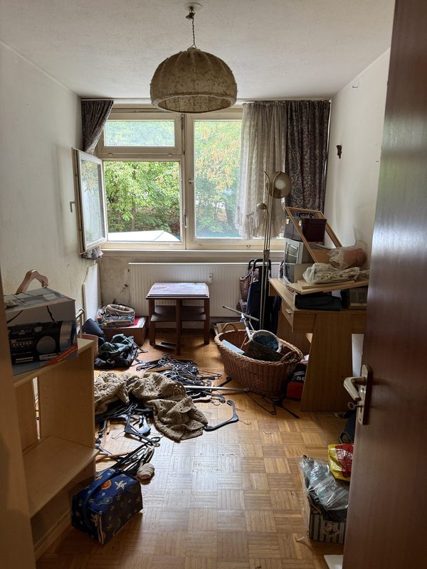 Zimmer vor der Räumung mit verteilten Kleiderbügeln, Körben und Kartons auf dem Boden