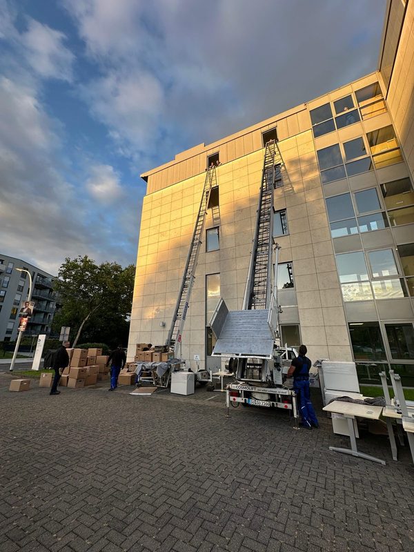 Zwei Möbellifte stehen ausgefahren nebeneinander an der Fassade eines Bürogebäudes